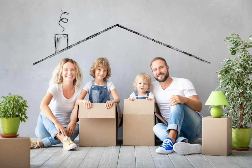 Eine vierköpfige Familie sitzt glücklich auf dem Boden zwischen Umzugskartons